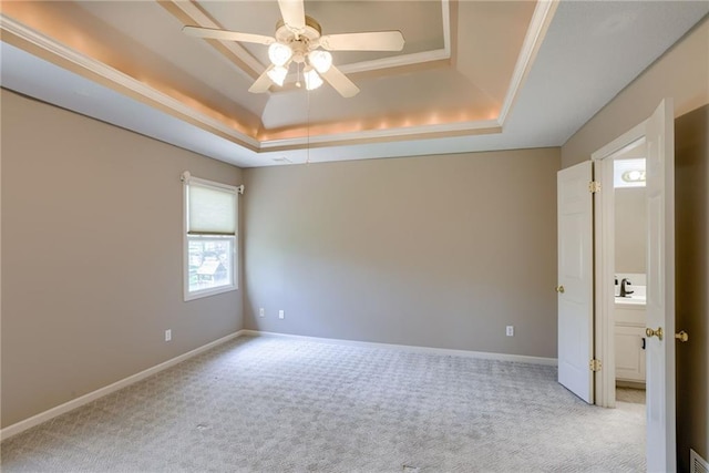unfurnished room featuring a raised ceiling, carpet floors, a ceiling fan, and baseboards