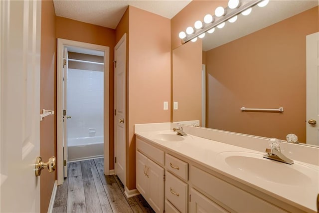 bathroom with baseboards, wood finished floors, a sink, and double vanity