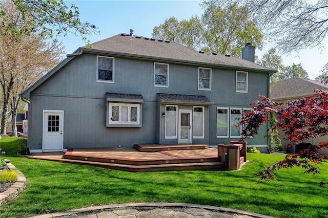 back of house with a yard, roof with shingles, a chimney, and a deck