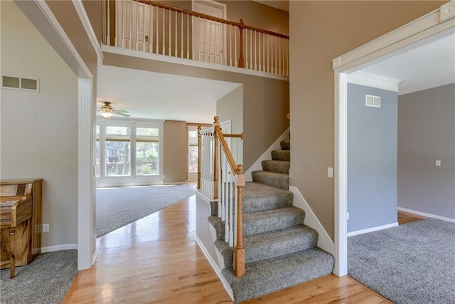 stairway with baseboards, wood finished floors, visible vents, and ceiling fan