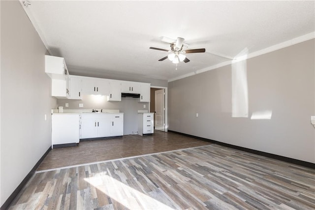 unfurnished living room with wood finished floors, ceiling fan, crown molding, and baseboards