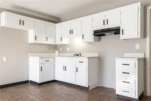 kitchen with baseboards, under cabinet range hood, a sink, white cabinetry, and a textured ceiling