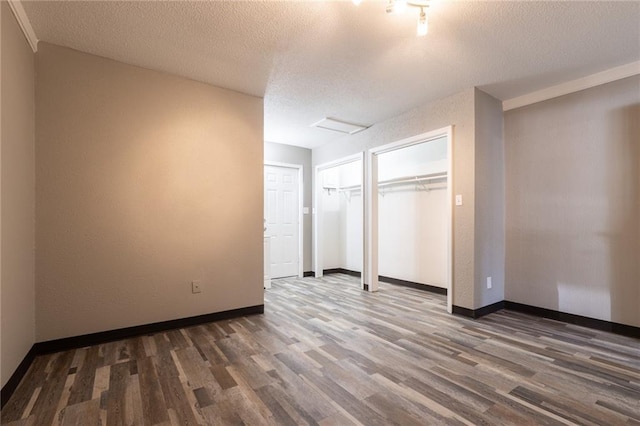 unfurnished bedroom with a textured ceiling, wood finished floors, multiple closets, and baseboards