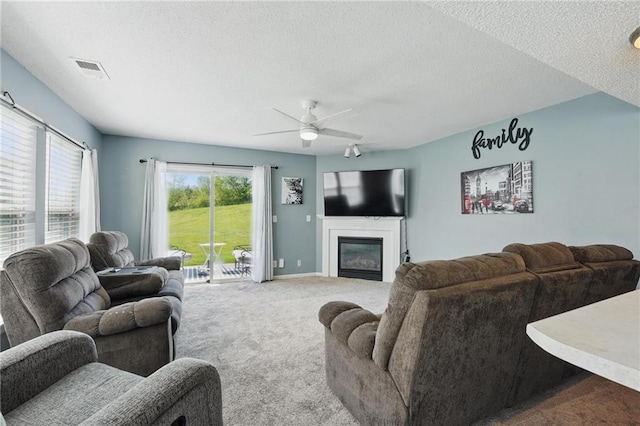 living room featuring a ceiling fan, a textured ceiling, a glass covered fireplace, carpet flooring, and baseboards