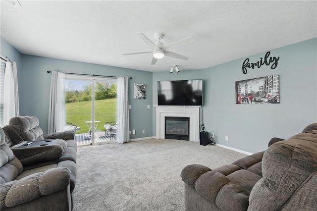 carpeted living area featuring a glass covered fireplace, a textured ceiling, a ceiling fan, and baseboards