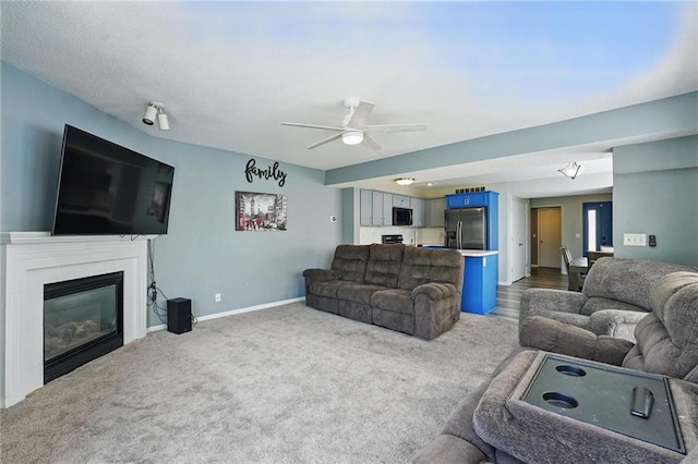 carpeted living room with ceiling fan, a glass covered fireplace, and baseboards