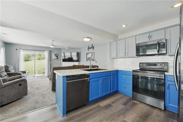 kitchen featuring stainless steel appliances, open floor plan, a sink, blue cabinets, and a textured ceiling