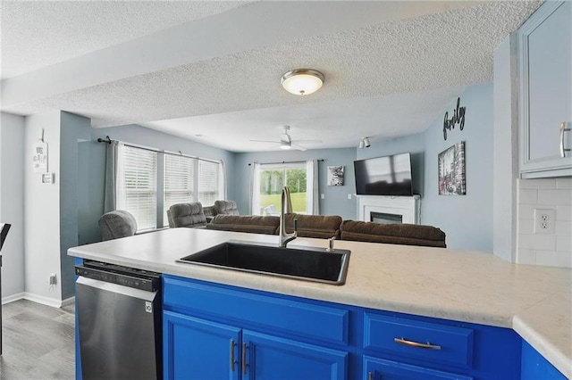 kitchen with blue cabinetry, dishwasher, a sink, open floor plan, and a textured ceiling