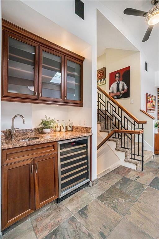 bar with stairs, beverage cooler, ceiling fan, a sink, and bar area