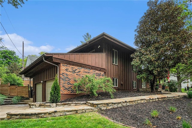 view of side of home featuring board and batten siding, brick siding, fence, concrete driveway, and an attached garage