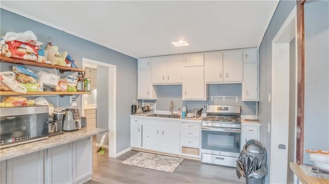 812 Pacific Ave, Osawatomie, KS 66064 - kitchen with stainless steel range with gas stovetop, light countertops, light wood-type flooring, white cabinetry, and crown molding