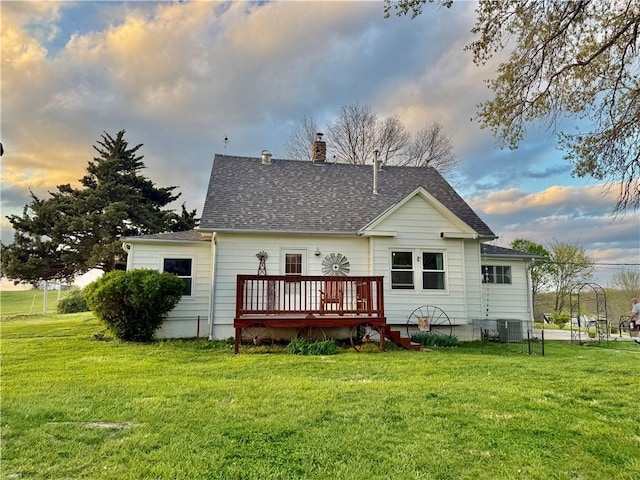 back of house at dusk featuring a deck, a chimney, a shingled roof, and a lawn