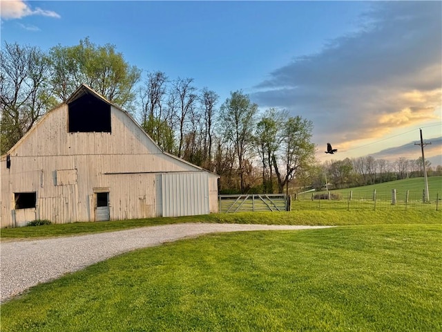 outdoor structure at dusk with driveway, a barn, an outbuilding, fence, and a yard
