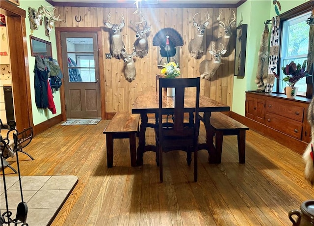 dining area featuring hardwood / wood-style floors, baseboards, a healthy amount of sunlight, and wood walls