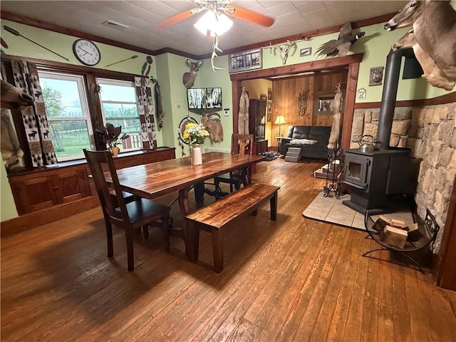 dining room with visible vents, hardwood / wood-style flooring, ceiling fan, and a wood stove