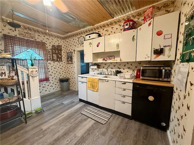 kitchen with wood finished floors, stainless steel microwave, wallpapered walls, black dishwasher, and light countertops