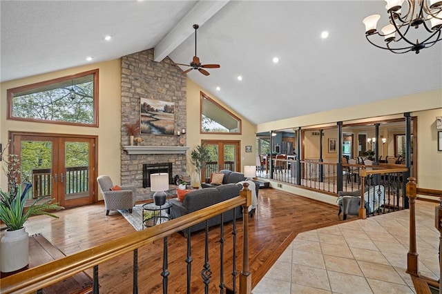 living area featuring high vaulted ceiling, beam ceiling, french doors, a stone fireplace, and ceiling fan
