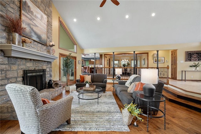 living area featuring ceiling fan, high vaulted ceiling, wood finished floors, a stone fireplace, and recessed lighting