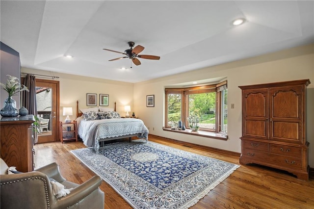 bedroom featuring multiple windows, a tray ceiling, light wood finished floors, and recessed lighting