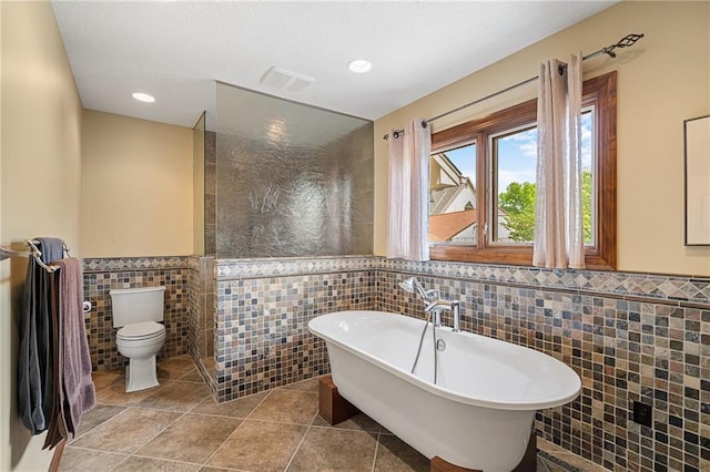 bathroom featuring tile walls, wainscoting, toilet, a freestanding bath, and recessed lighting