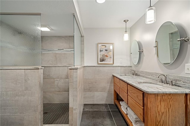 bathroom featuring a walk in shower, double vanity, tile patterned floors, tile walls, and wainscoting