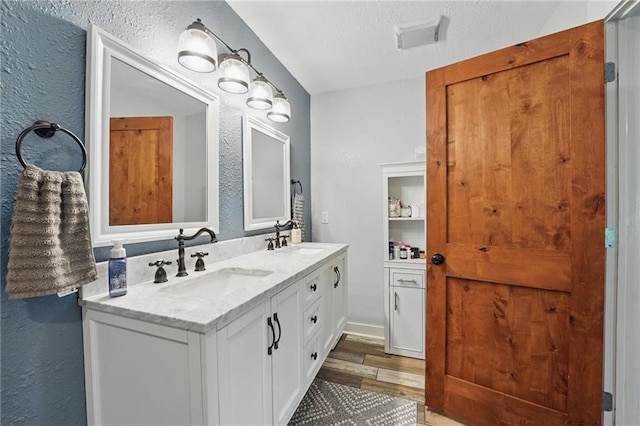 full bath with a sink, a textured wall, and wood finished floors