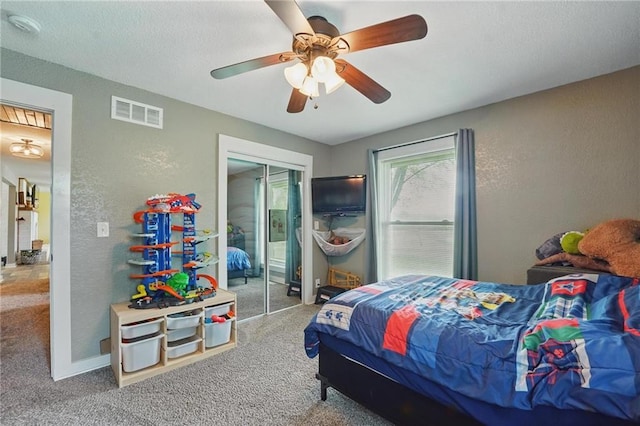 carpeted bedroom featuring a textured wall, a closet, ceiling fan, and visible vents