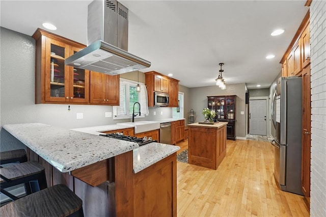 kitchen with a peninsula, island range hood, a center island, brown cabinets, and stainless steel appliances