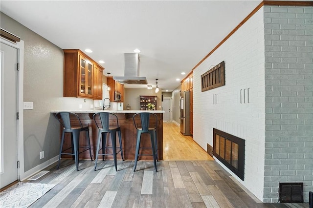 kitchen featuring visible vents, brown cabinetry, a peninsula, a fireplace, and stainless steel appliances