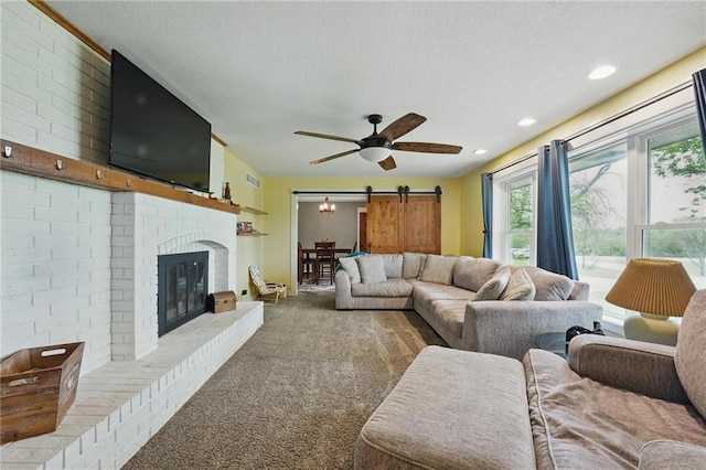 carpeted living area with visible vents, a barn door, a textured ceiling, and a brick fireplace