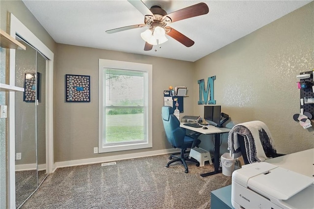 carpeted office space featuring a ceiling fan, a textured wall, visible vents, and baseboards