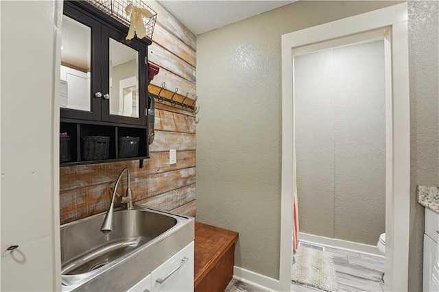bar with baseboards, a textured wall, and a sink