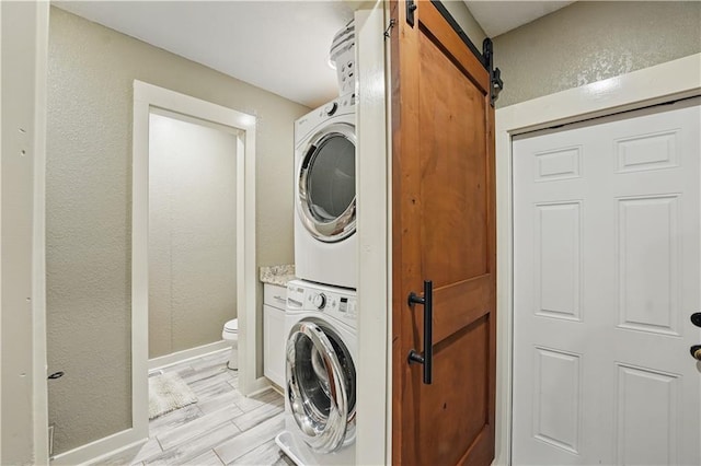 laundry area featuring baseboards, a textured wall, stacked washer / drying machine, and a barn door