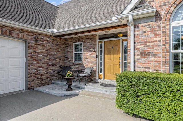 view of exterior entry with a shingled roof, brick siding, and a garage