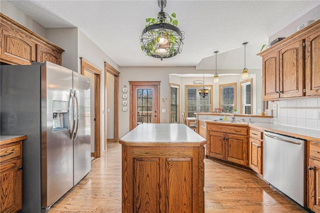 kitchen featuring a sink, light wood-style floors, an inviting chandelier, appliances with stainless steel finishes, and a kitchen island
