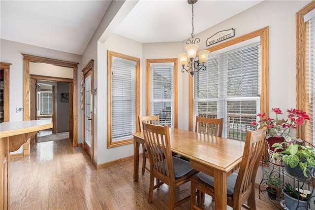 dining area featuring light wood finished floors, baseboards, and a notable chandelier