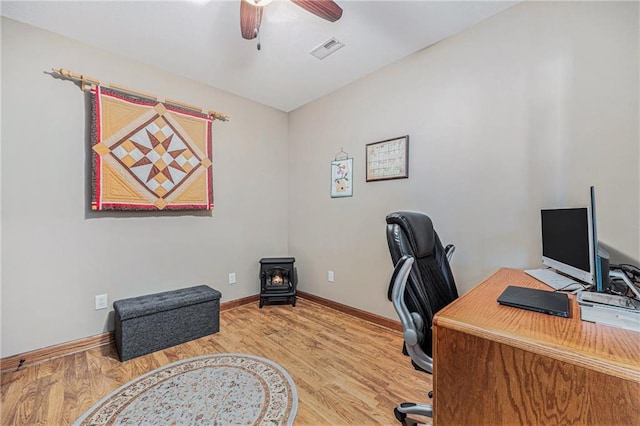office space with wood finished floors, a wood stove, ceiling fan, and visible vents