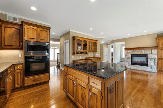 5108 W 150th St, Leawood, KS 66224 - kitchen featuring black appliances, crown molding, wood finished floors, brown cabinetry, and a fireplace