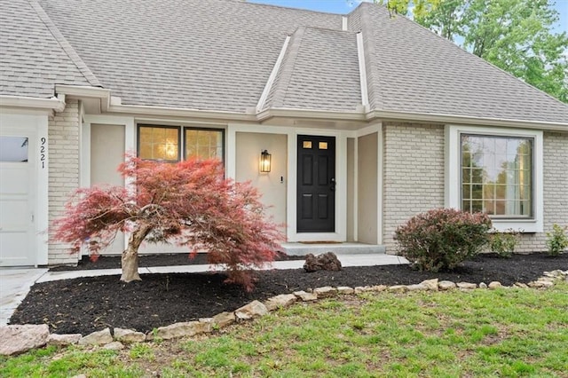 entrance to property featuring brick siding, an attached garage, and roof with shingles