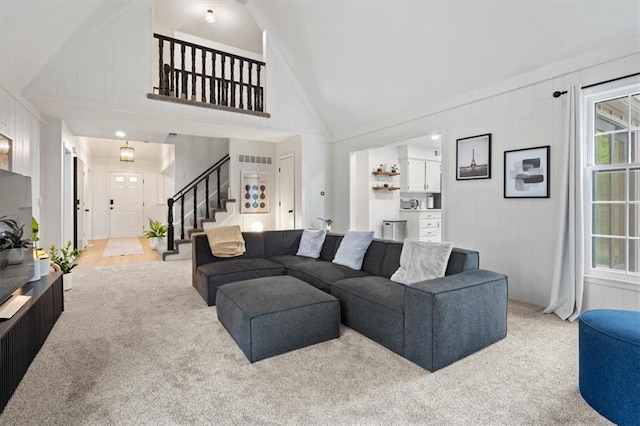 living area with plenty of natural light, carpet flooring, stairs, and high vaulted ceiling