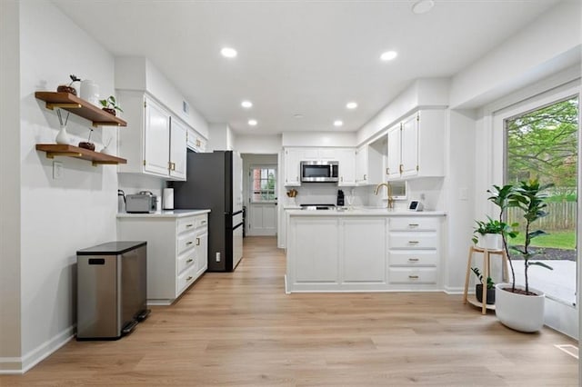 kitchen with light countertops, white cabinetry, stainless steel microwave, and open shelves