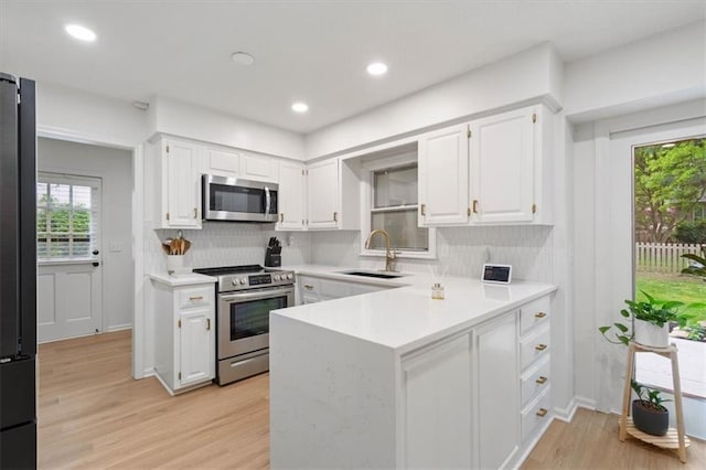 kitchen with white cabinets, stainless steel appliances, a sink, and light wood-style floors