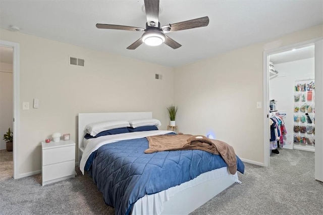 carpeted bedroom with a walk in closet, ceiling fan, baseboards, and visible vents