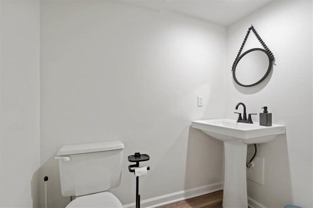 half bathroom with baseboards, toilet, and wood finished floors