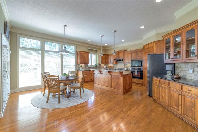 kitchen featuring a kitchen breakfast bar, under cabinet range hood, brown cabinets, backsplash, and black appliances