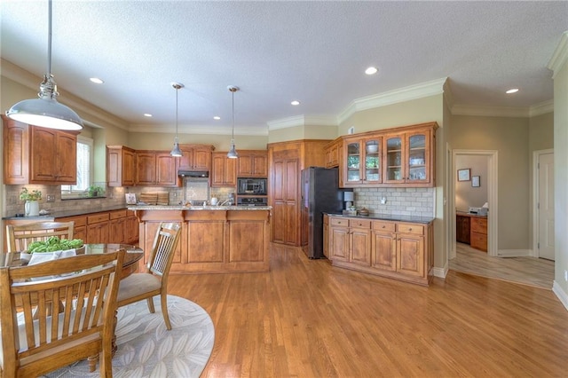 kitchen with a kitchen island with sink, brown cabinetry, black microwave, freestanding refrigerator, and light wood finished floors