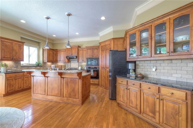 kitchen featuring backsplash, glass insert cabinets, black appliances, and a kitchen bar