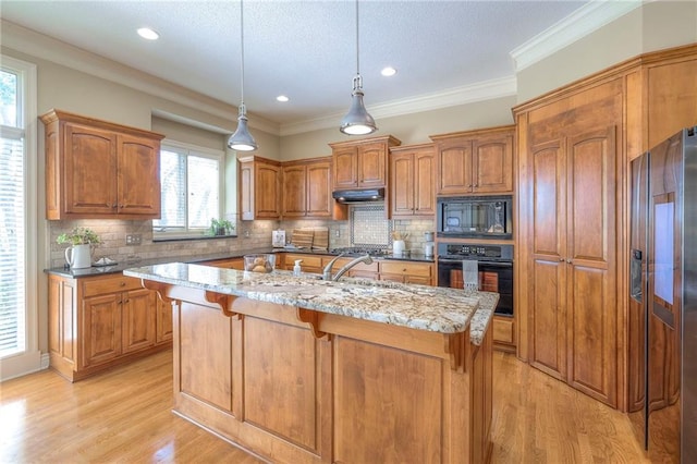 kitchen with decorative backsplash, black appliances, brown cabinets, and an island with sink