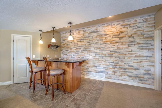 bar featuring visible vents, baseboards, a textured ceiling, dark tile patterned flooring, and wet bar