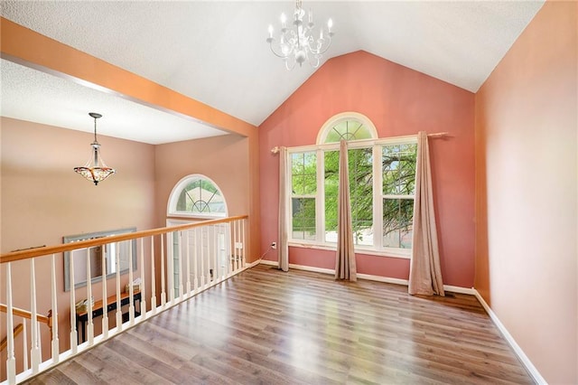 spare room featuring an inviting chandelier, baseboards, lofted ceiling, and wood finished floors